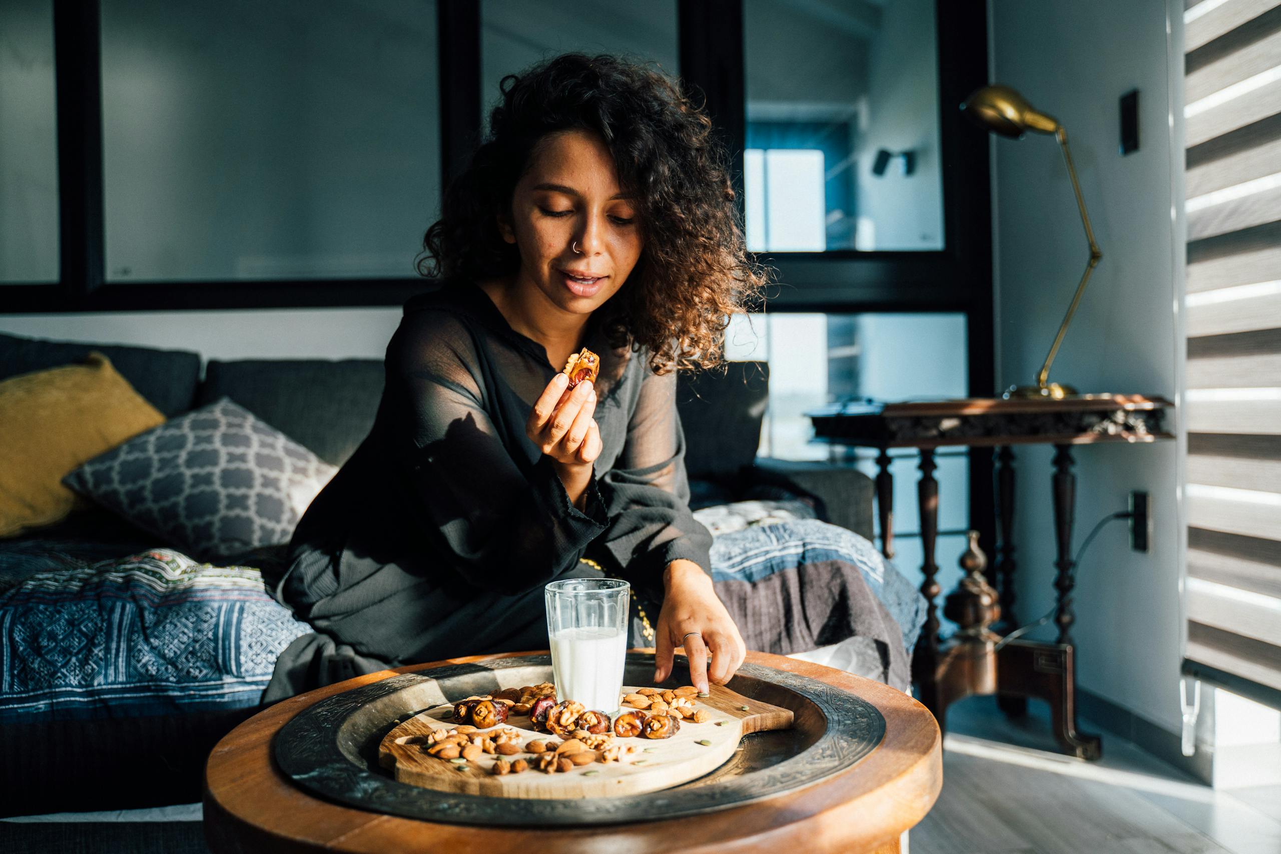 A woman enjoying a healthy snack of nuts and dates on a stylish platter in a cozy living room.