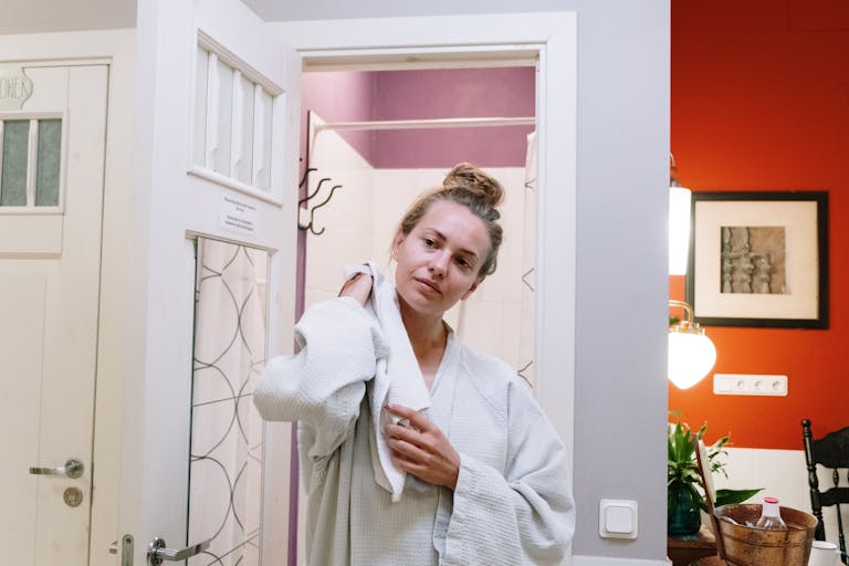 A woman in a bathrobe drying off after a shower in a cozy home bathroom.
