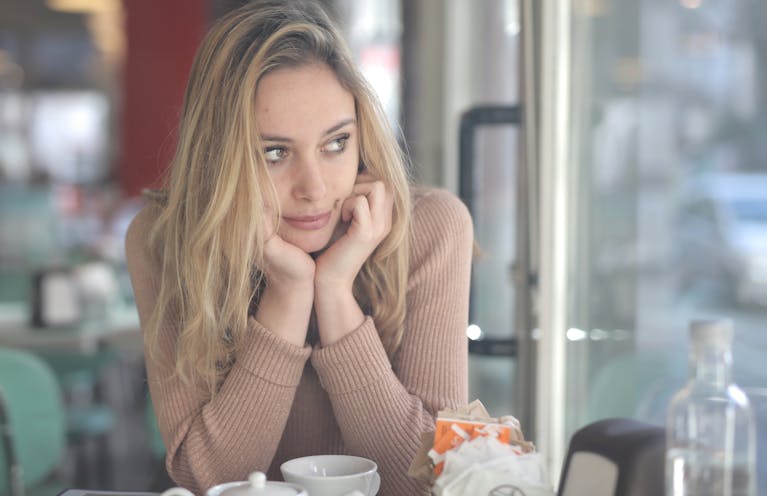 A woman in a cafe looking contemplative with a coffee cup nearby, captured with Canon EOS 5DS.