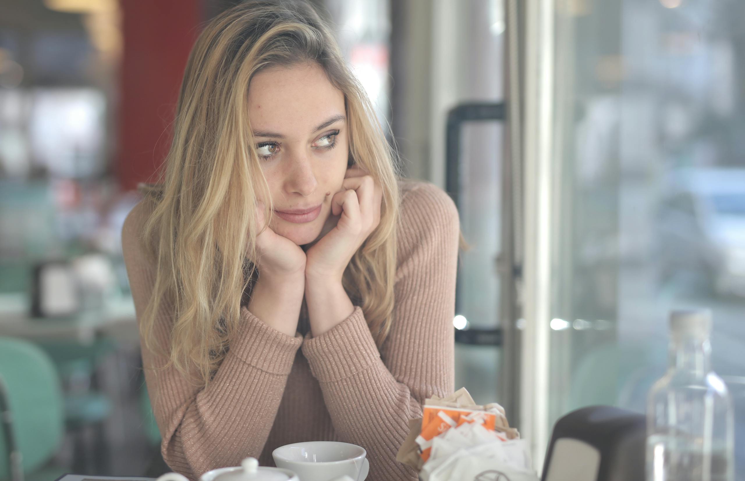 A woman in a cafe looking contemplative with a coffee cup nearby, captured with Canon EOS 5DS.