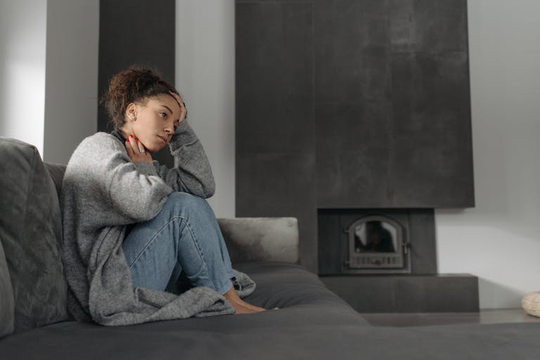 A woman in a cozy living room feeling unwell, sitting on a sofa with a thoughtful expression.