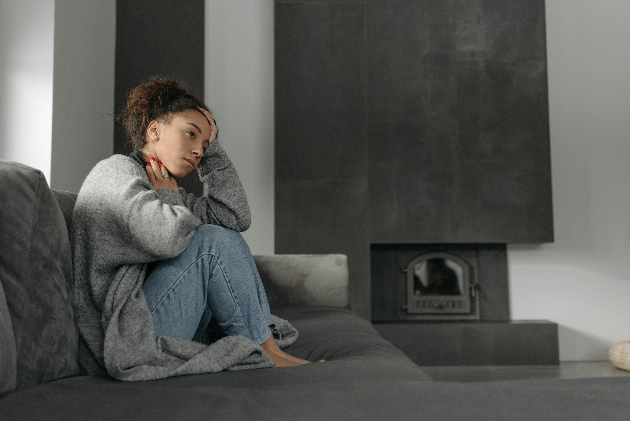 A woman in a cozy living room feeling unwell, sitting on a sofa with a thoughtful expression.