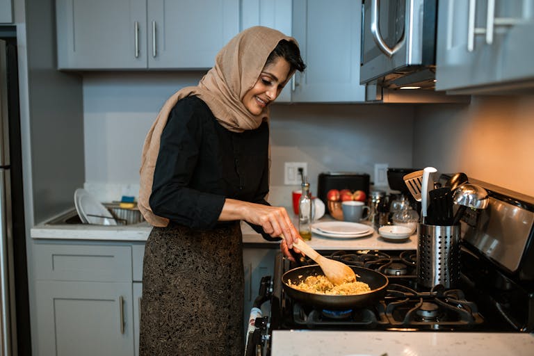A woman in a hijab cooking fried rice in a contemporary kitchen setting.