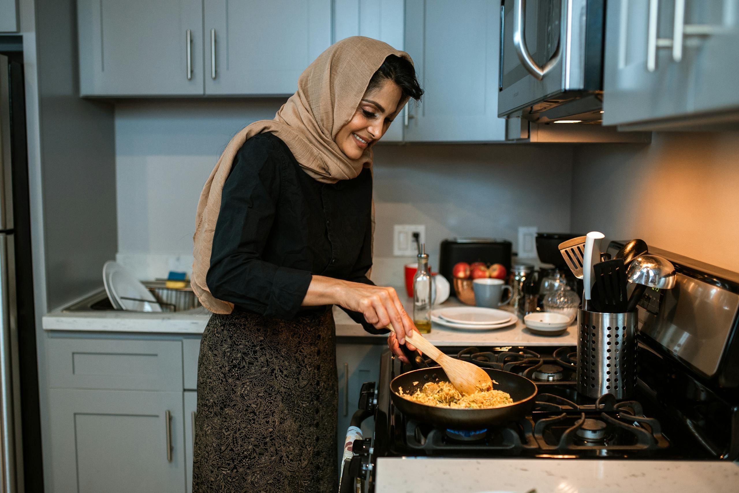 A woman in a hijab cooking fried rice in a contemporary kitchen setting.