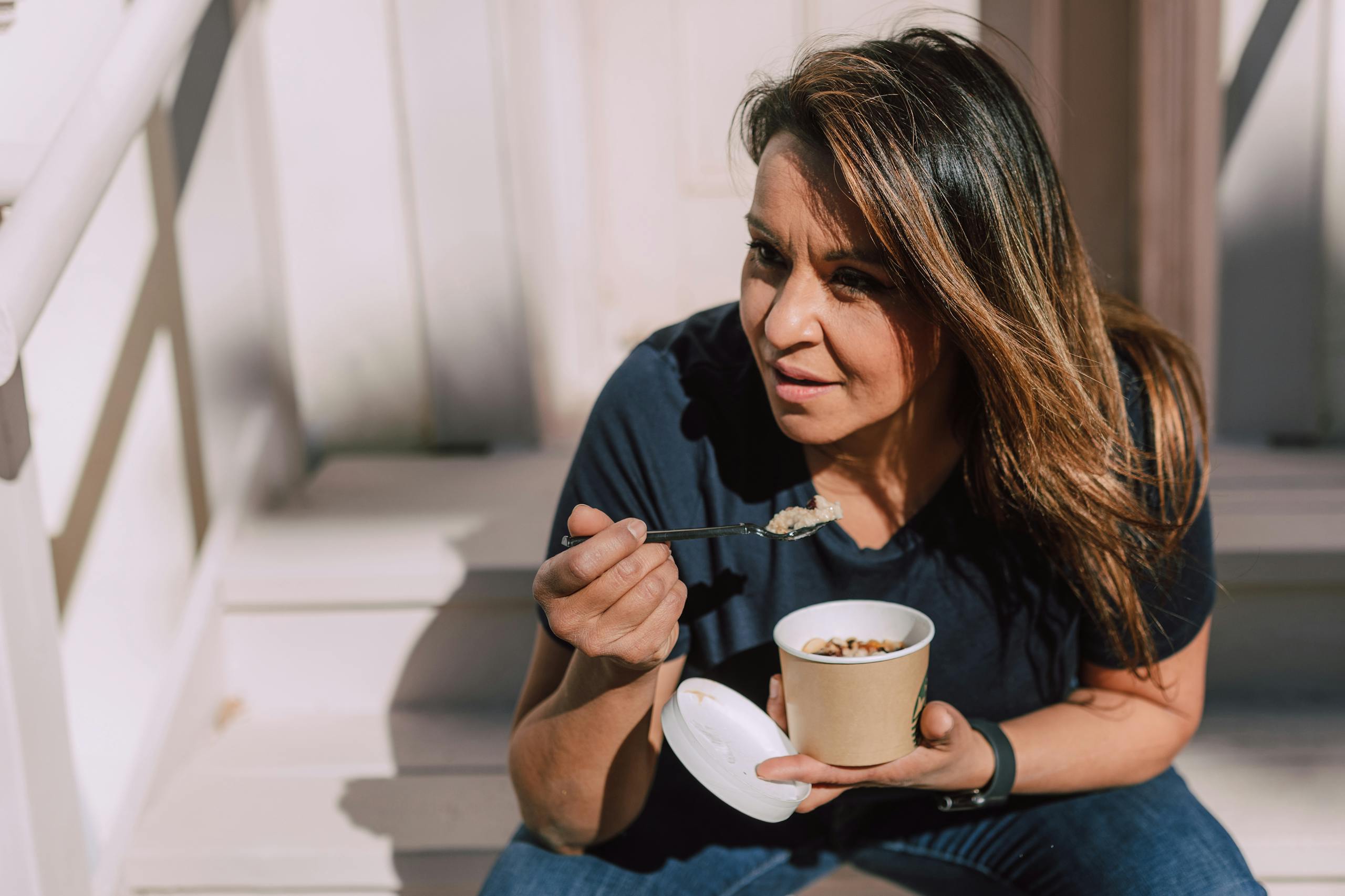 A woman in casual wear eating oats from a disposable bowl while sitting outdoors. Healthy lifestyle concept.