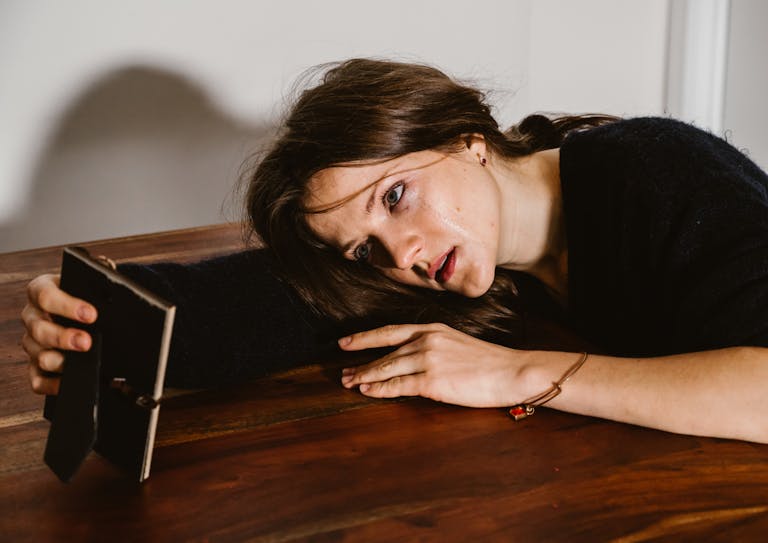 A woman in emotional distress lays on a wooden table holding a picture frame.