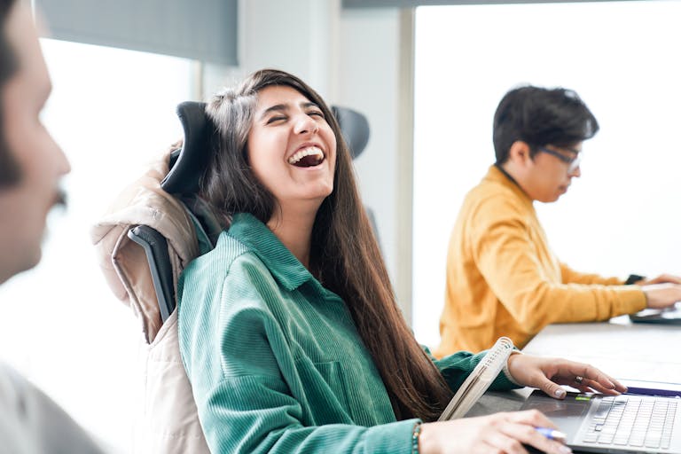 A woman laughs heartily while sitting in a Tehran office, creating a cheerful atmosphere.