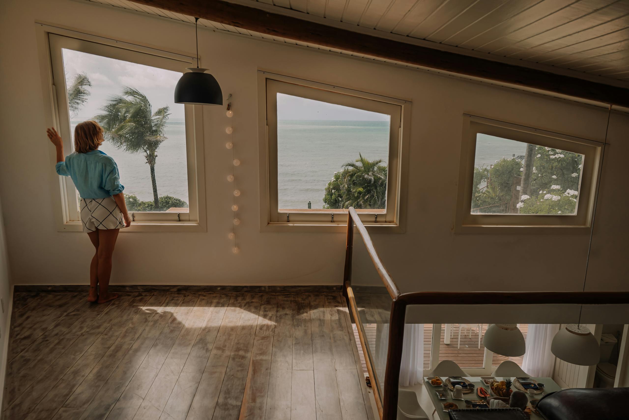 A woman looks out at the ocean view from a stylish modern home interior with large windows.