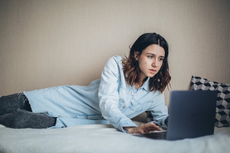 A woman relaxes in bed while working on a laptop, embodying freelance lifestyle and remote work convenience.