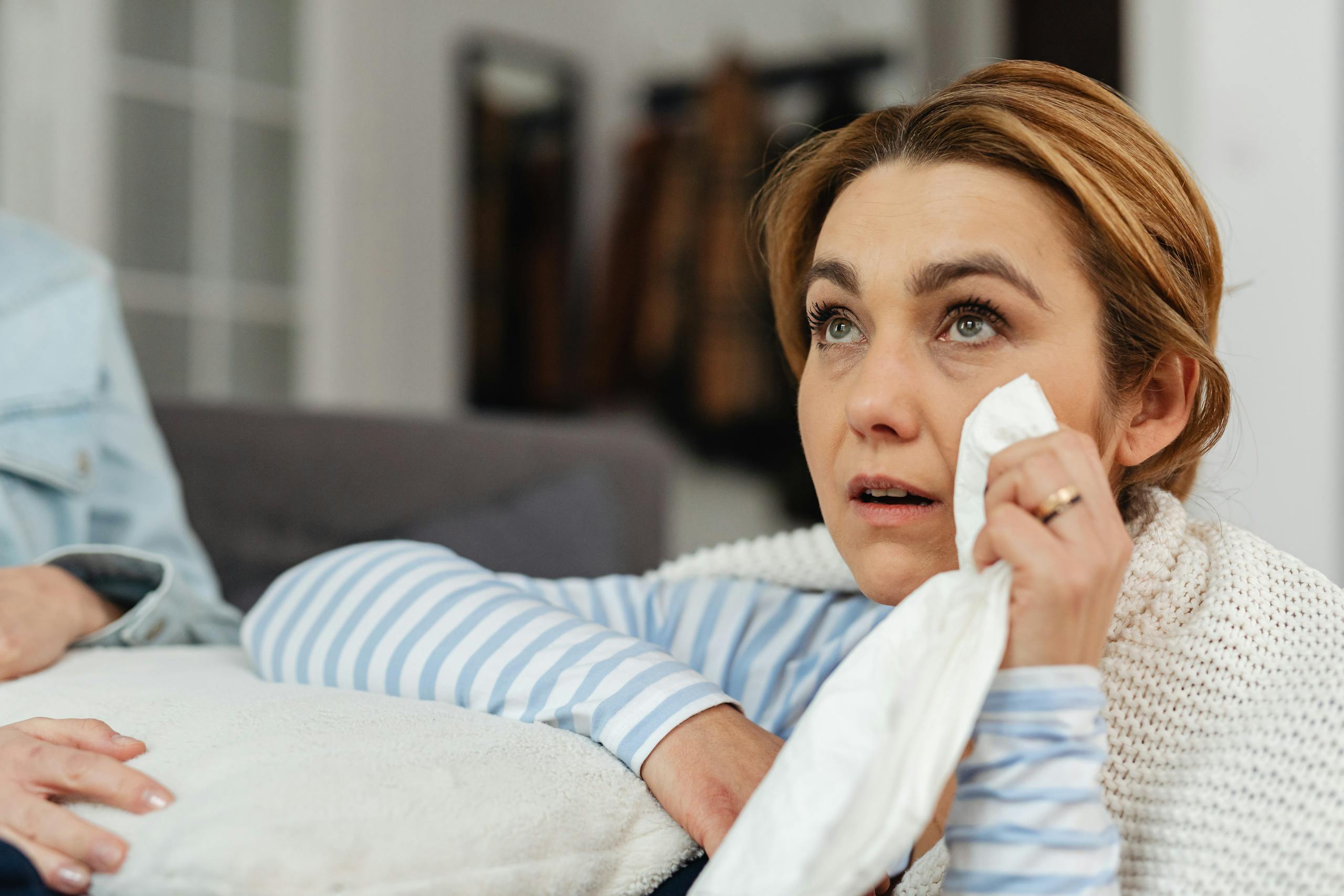 A woman wipes her tears with a tissue, expressing emotions while indoors.