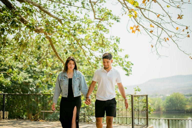 A young couple enjoying a sunny day, holding hands while walking outdoors.