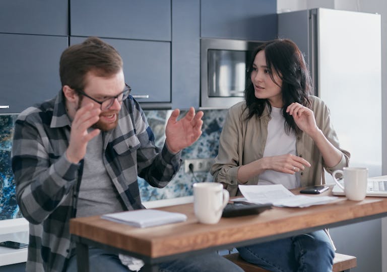 An upset couple discussing financial problems at their kitchen table, appearing anxious and concerned.