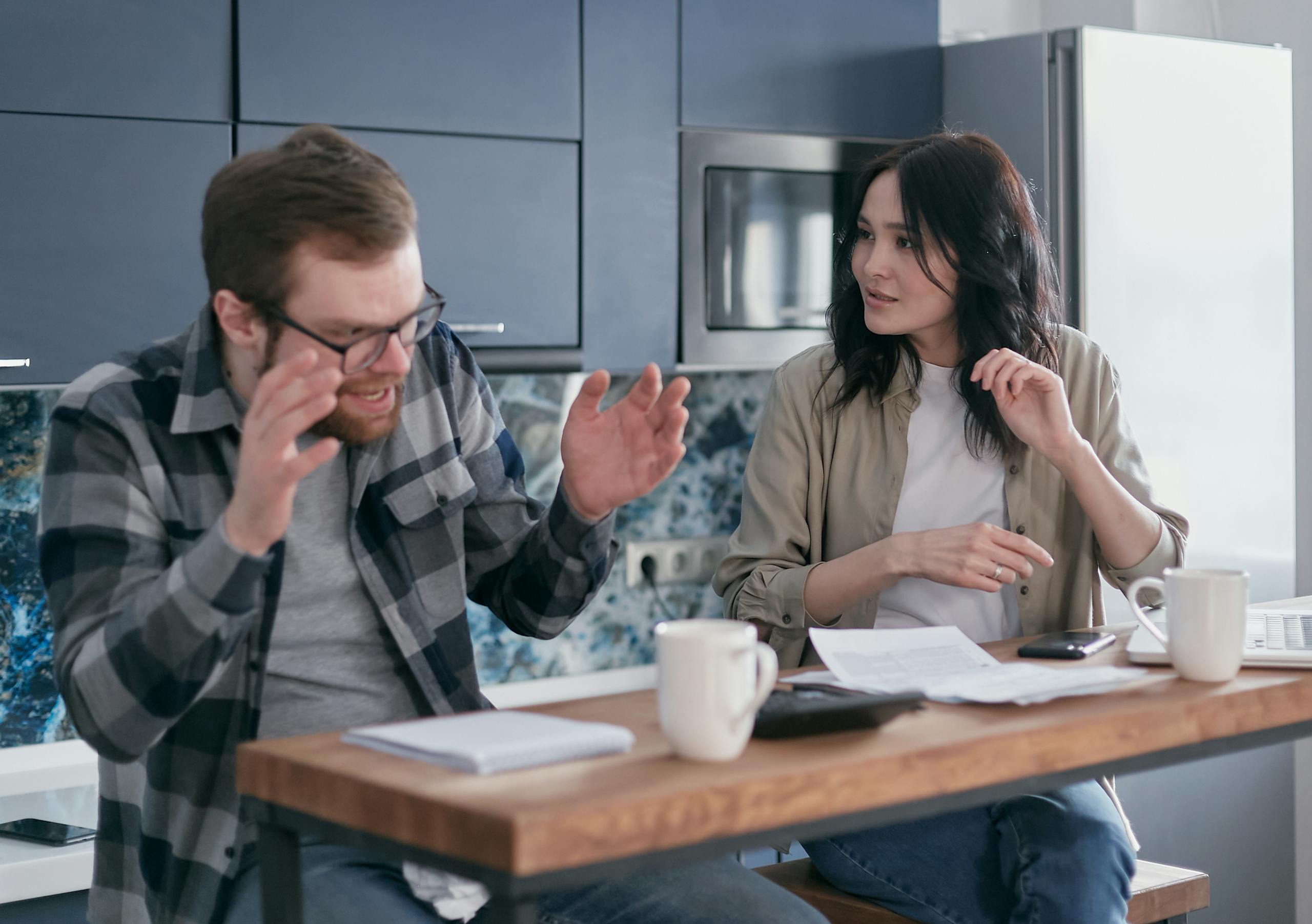 An upset couple discussing financial problems at their kitchen table, appearing anxious and concerned.