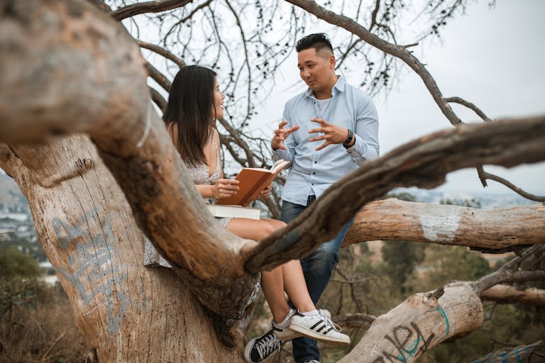 Asian couple enjoying a thoughtful conversation sitting on a tree branch outdoors.
