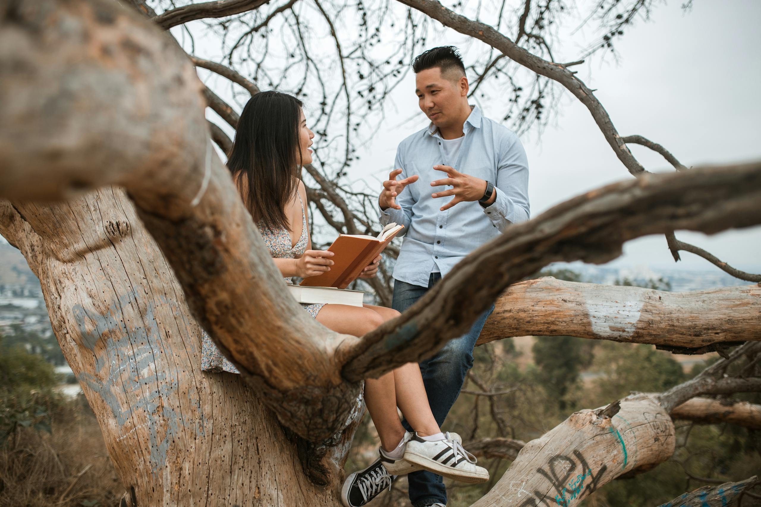 Asian couple enjoying a thoughtful conversation sitting on a tree branch outdoors.