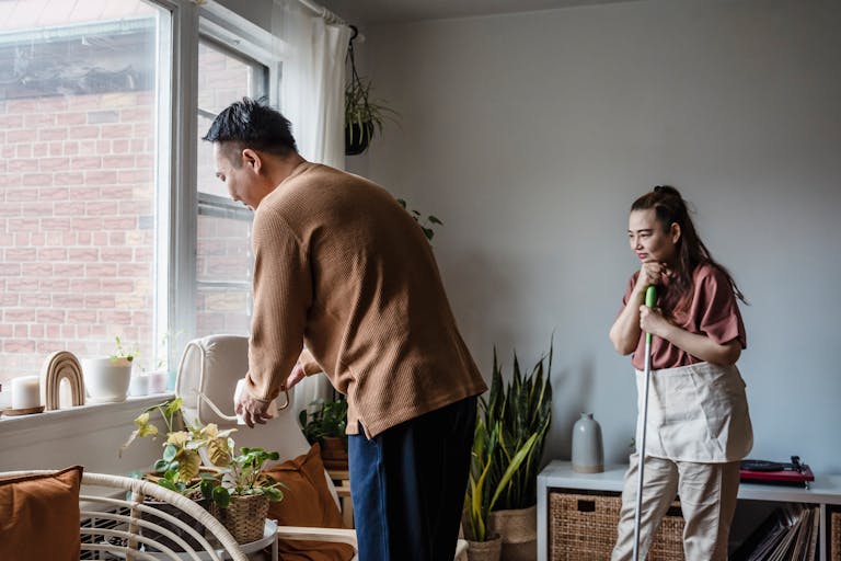 Asian couple tending to plants in a sunlit living room, enhancing their indoor oasis.