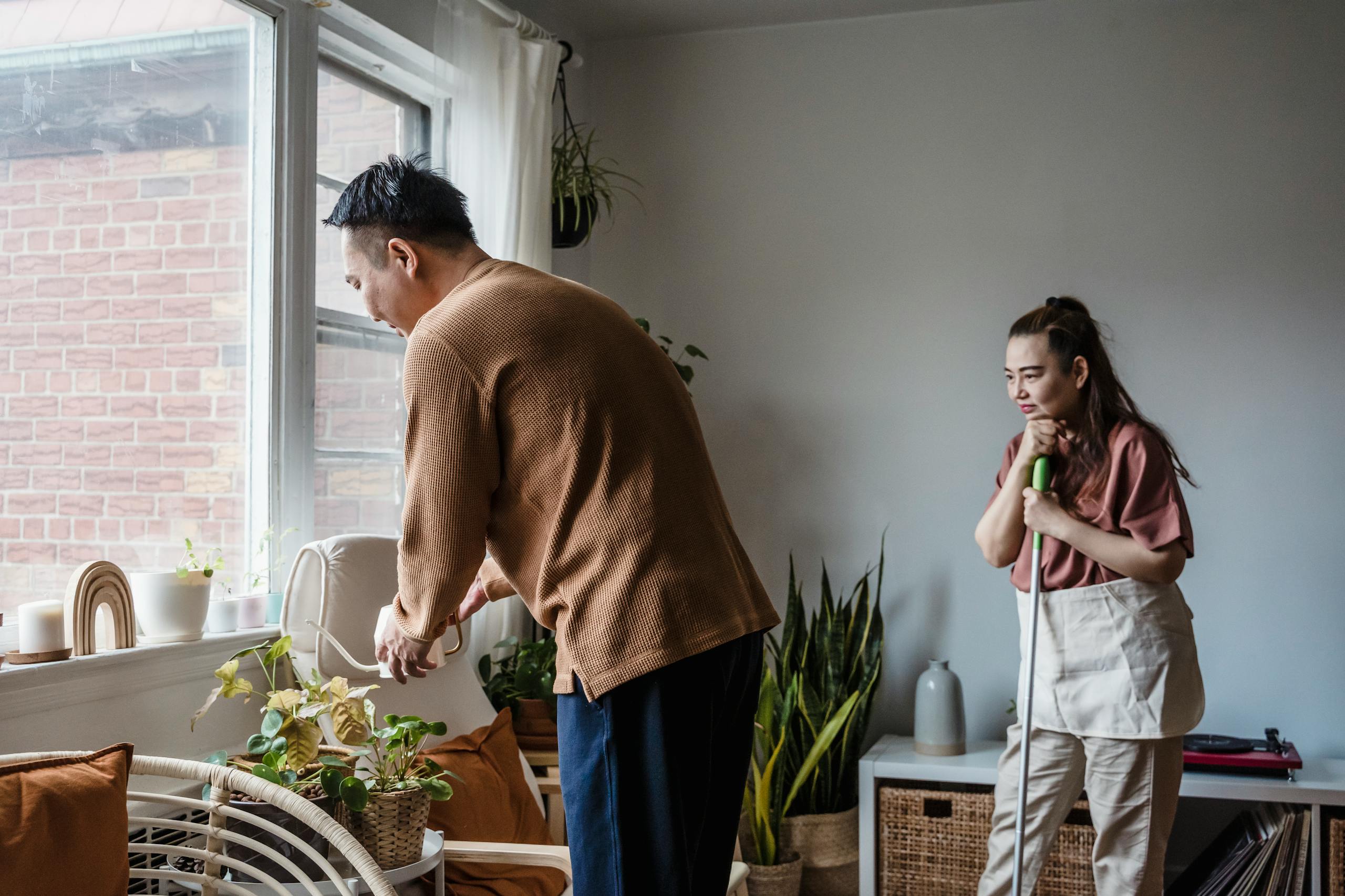 Asian couple tending to plants in a sunlit living room, enhancing their indoor oasis.
