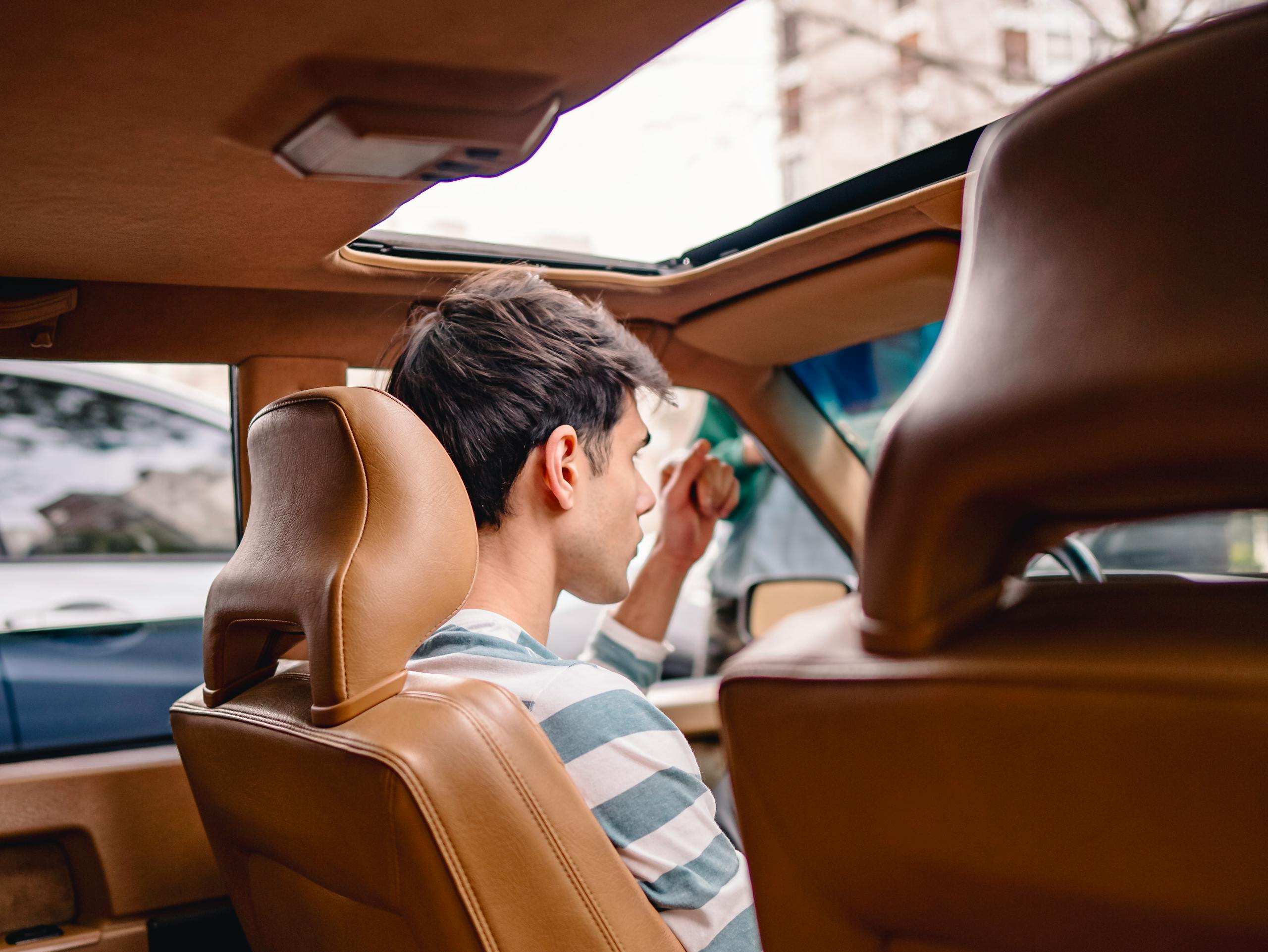Back view of a young man sitting in a vintage car with a sunroof, enjoying a sunny day.