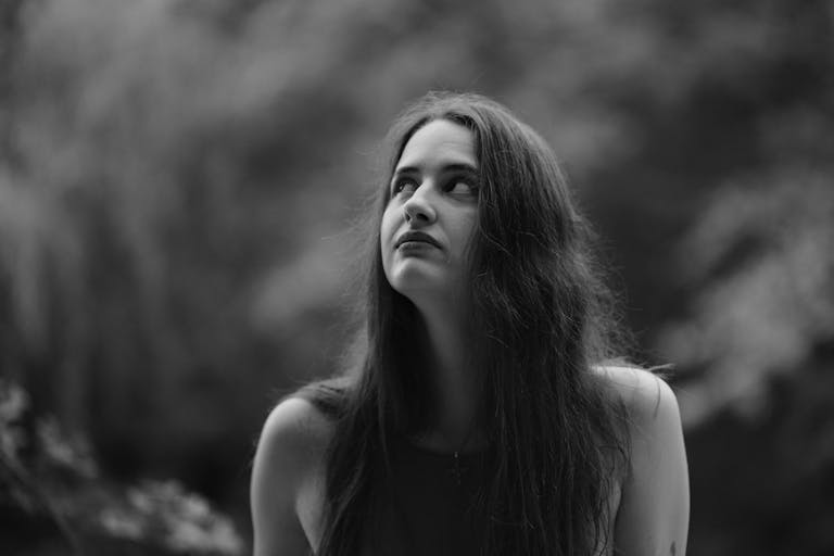 Black and white photo of a woman looking upwards in an outdoor setting.