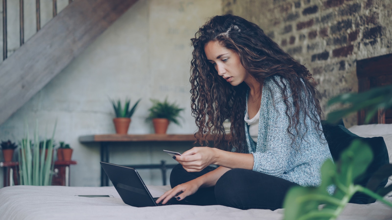 Woman using laptop and credit card on bed.