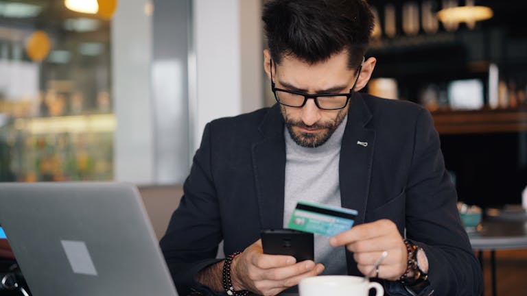 Businessman making online payment with smartphone and credit card in a modern café.