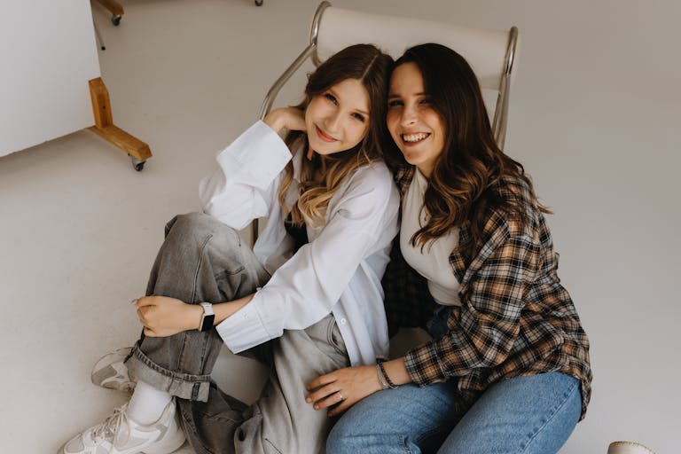 Casual and joyful moment of two women sitting comfortably indoors, sharing smiles.