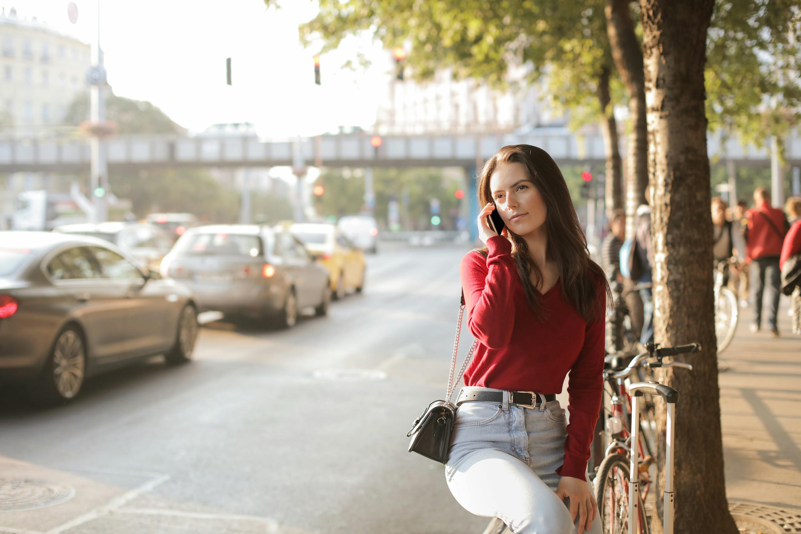 Casual woman in red sweater talking on phone by street with traffic.