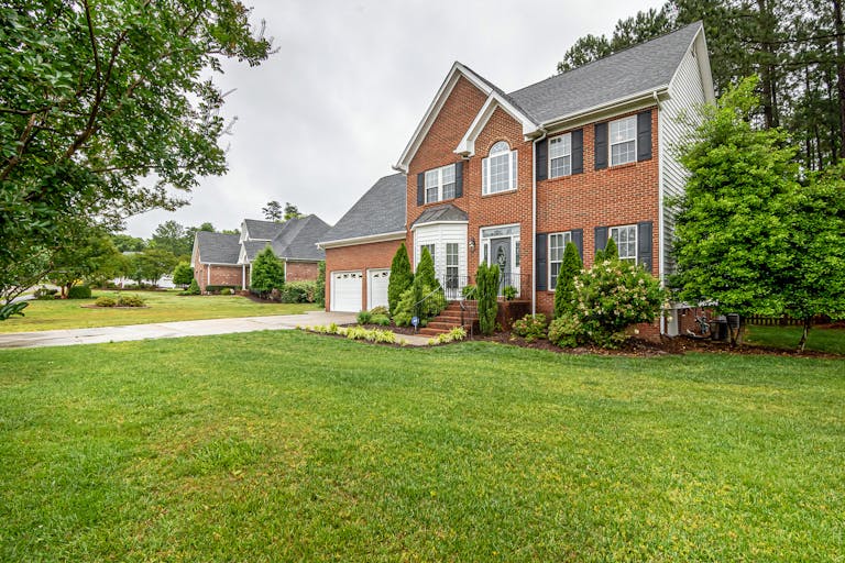 Charming two-story brick house with manicured lawn and trees, perfect family home.