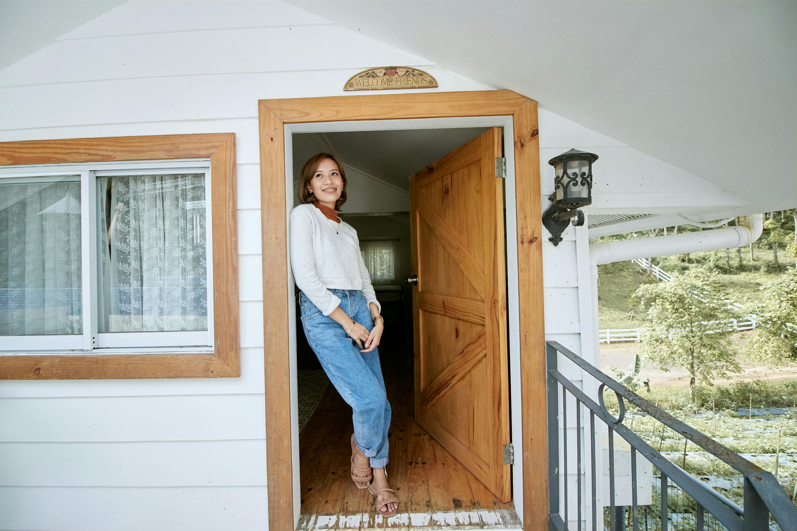 Cheerful woman standing at a cozy wooden doorway, enjoying a sunny day.