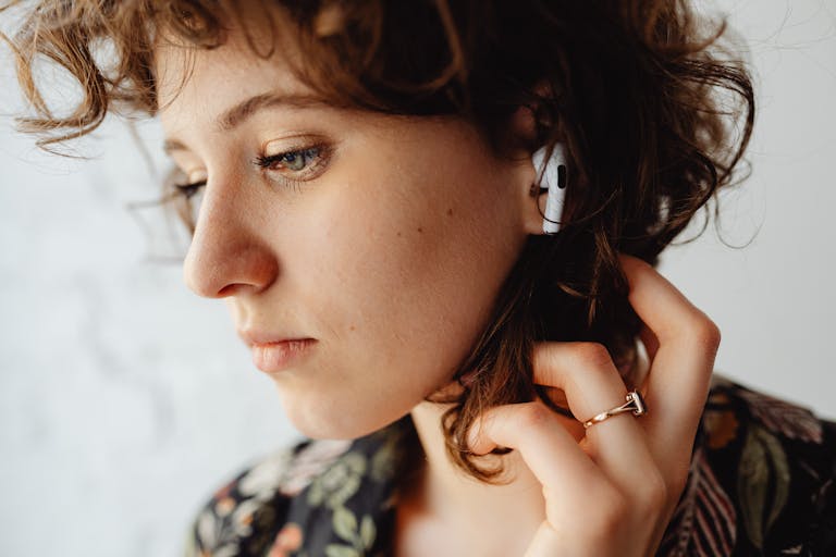 Close-up of a woman with curly hair listening to music using AirPods, showcasing technology and lifestyle.