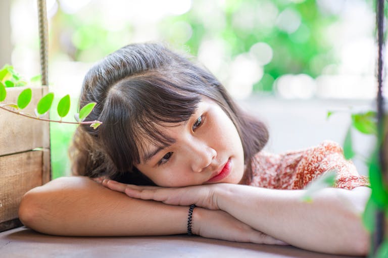 Close-up outdoor portrait of a thoughtful teenager resting on a table surrounded by leaves.