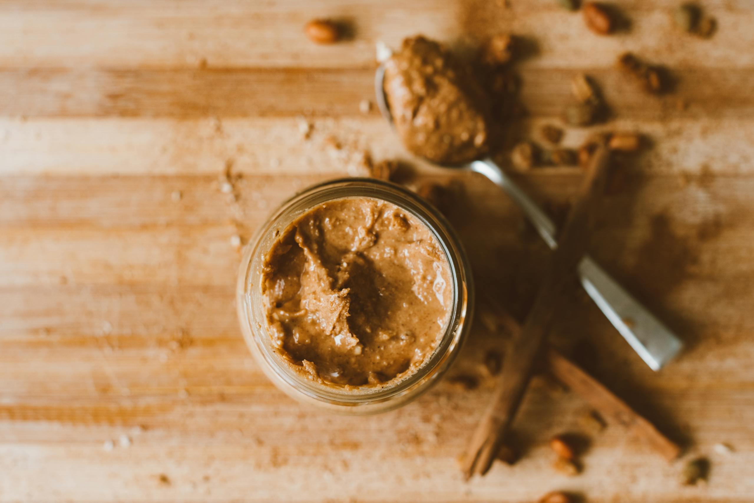 Creamy peanut butter in a jar with spoon on wooden surface, offering a rustic kitchen vibe.