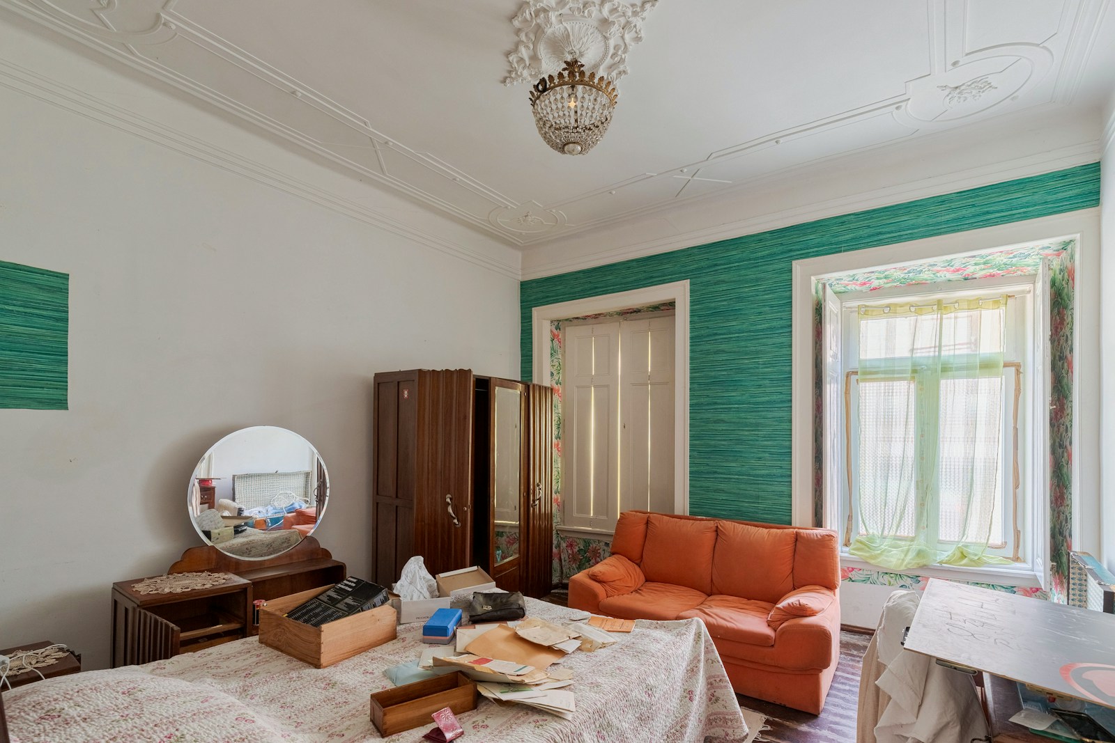 A cluttered bedroom with an orange sofa and vintage furniture.