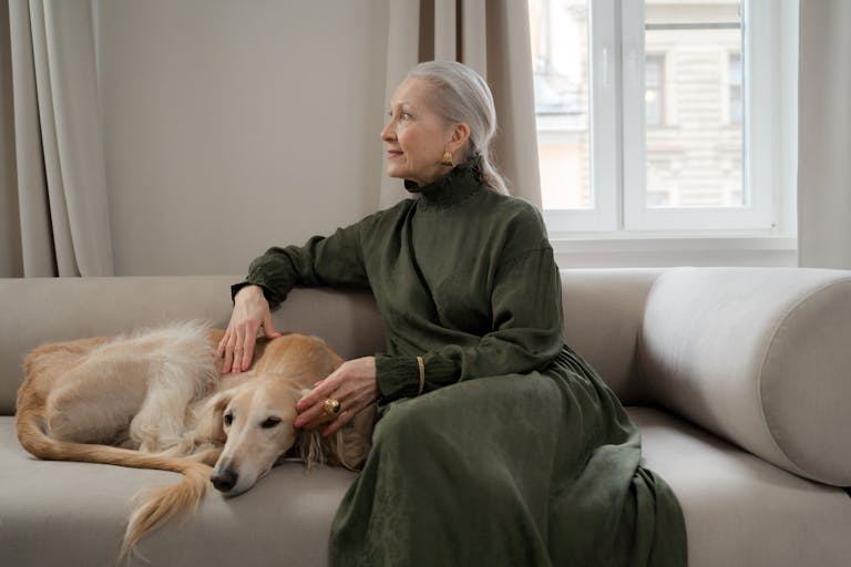 Elderly woman sitting with her greyhound on a sofa, enjoying a peaceful moment indoors.