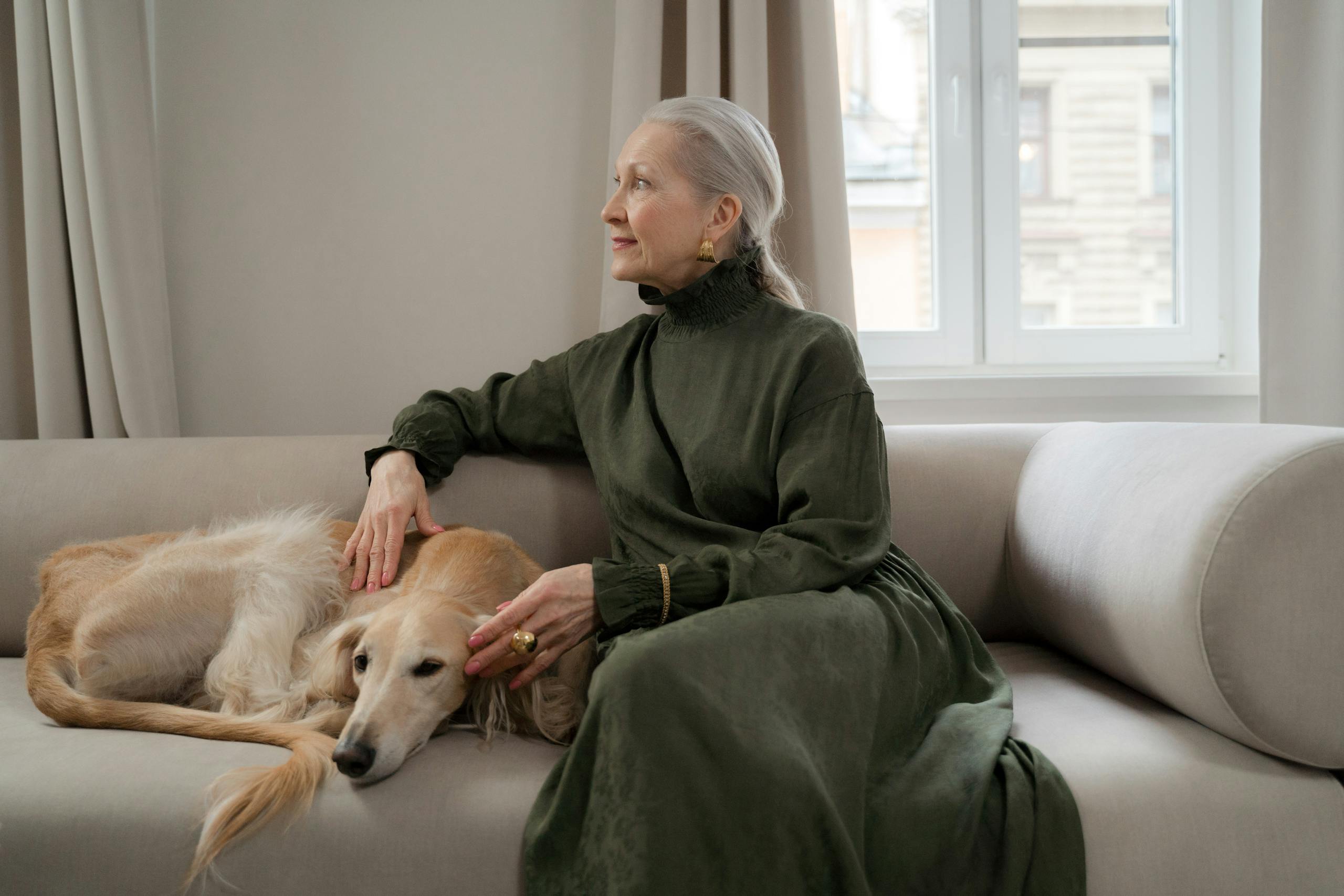 Elderly woman sitting with her greyhound on a sofa, enjoying a peaceful moment indoors.