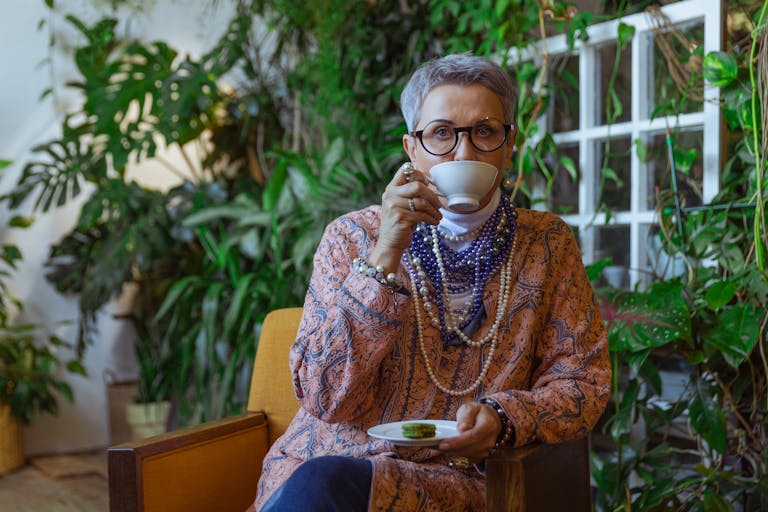 Elegant senior woman sipping tea in a lush green interior setting, showcasing style and tranquility.