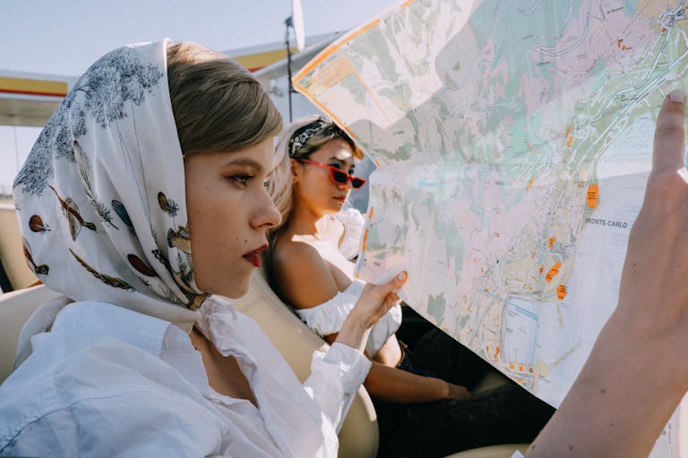 Elegant women on a road trip holding a map in a cabriolet under sunny skies.