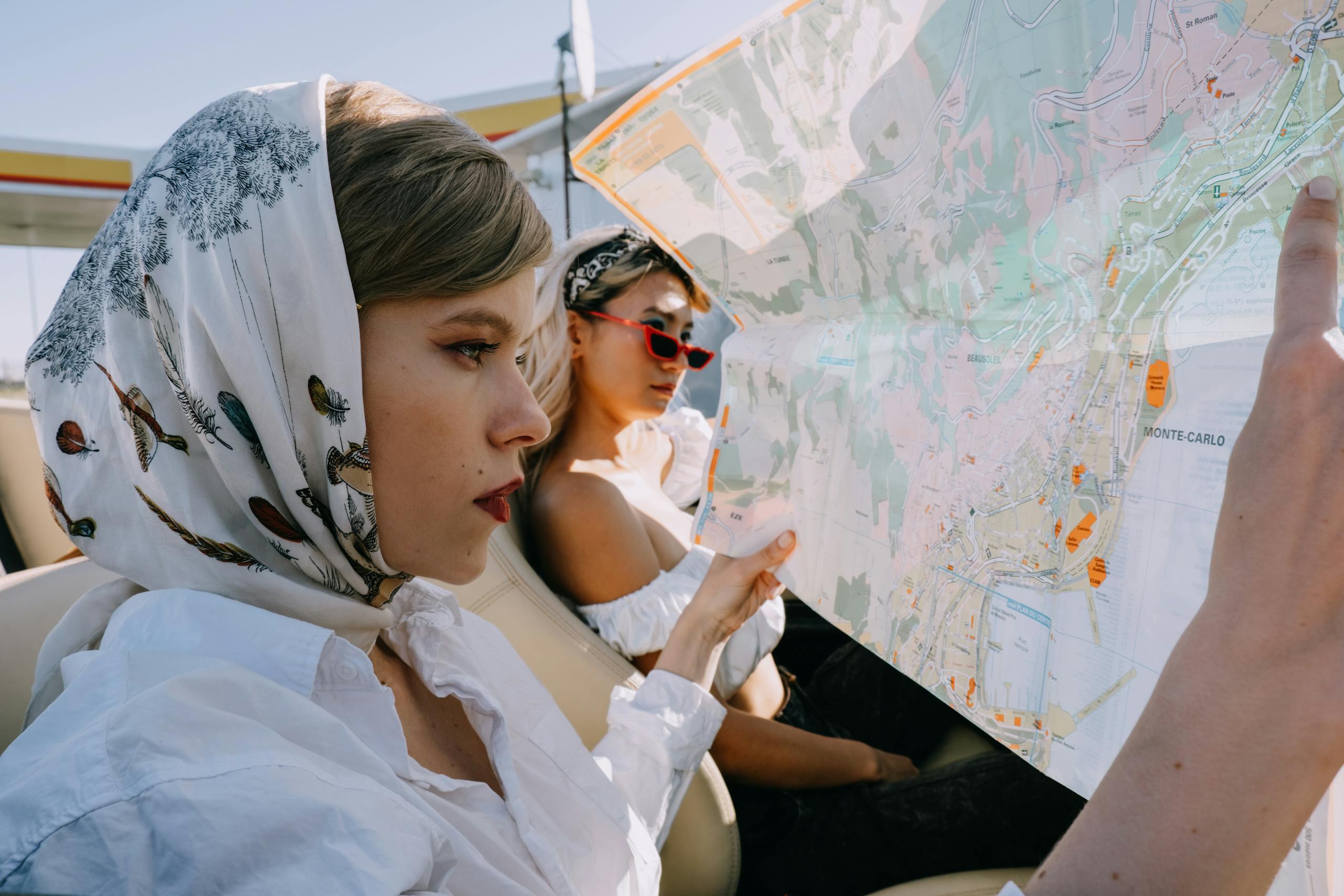 Elegant women on a road trip holding a map in a cabriolet under sunny skies.