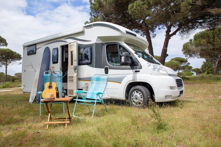 Explore the outdoor lifestyle with an RV, surfboards, and guitar in a serene Portuguese park.