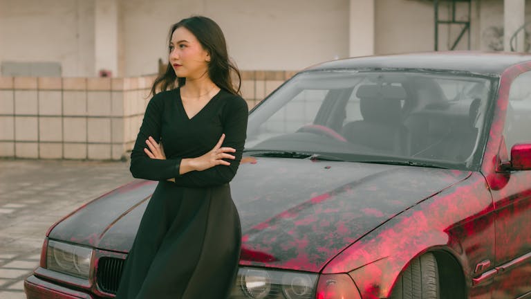 Fashionable woman in black attire posing confidently by a red car in an outdoor setting.