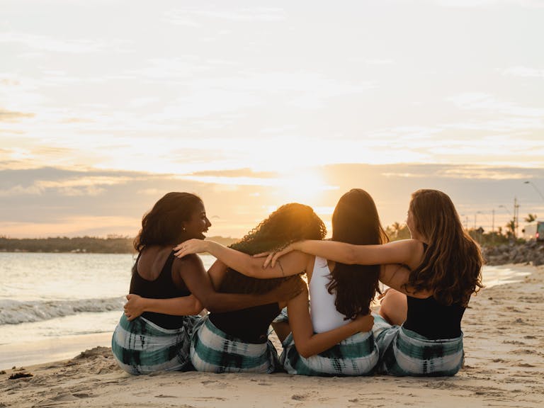 Four diverse women sitting together on a Brazilian beach, enjoying a sunset moment.