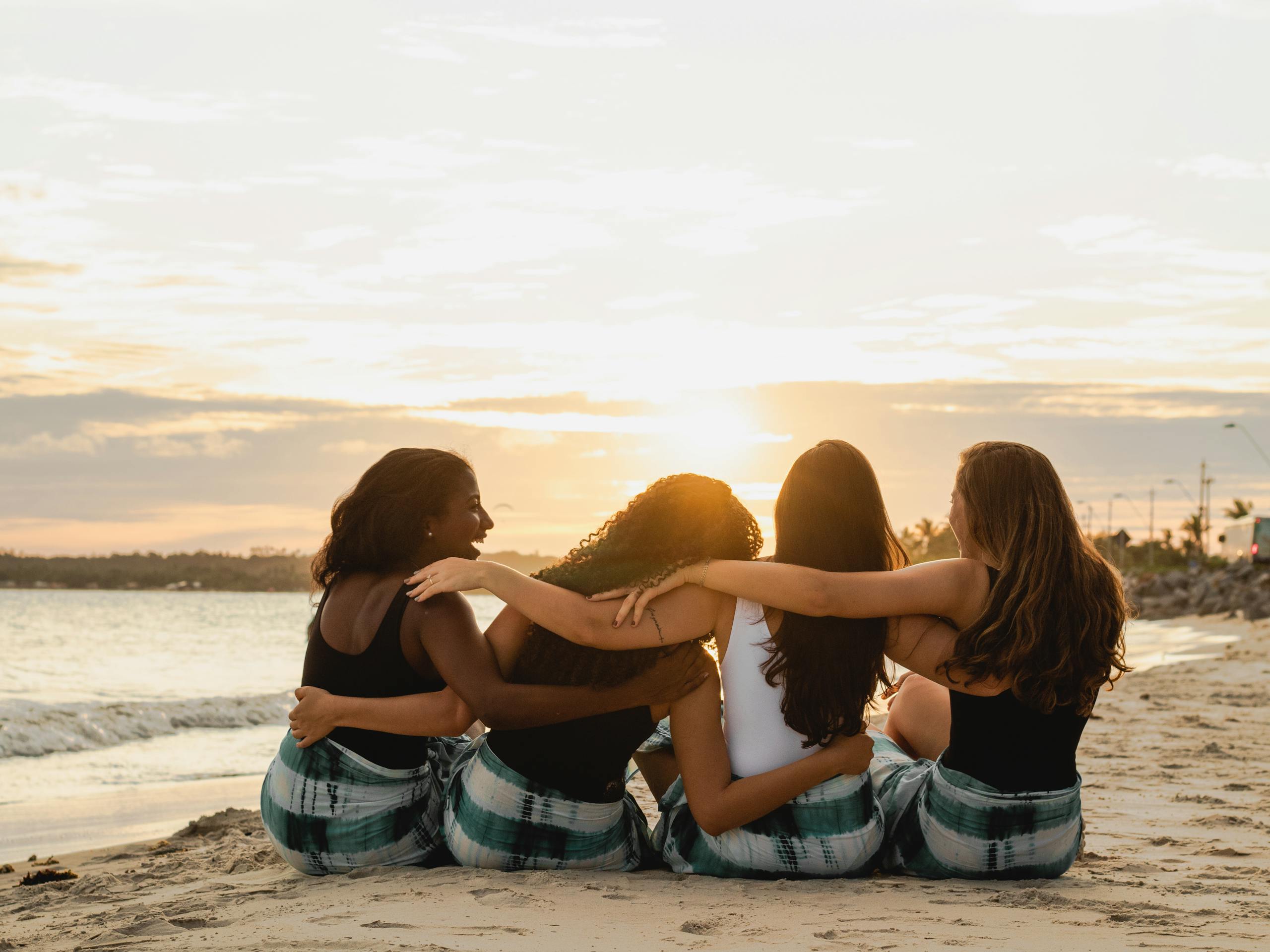 Four diverse women sitting together on a Brazilian beach, enjoying a sunset moment.