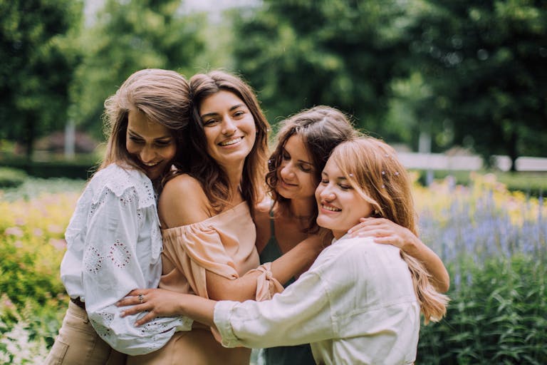 Four women joyfully embracing in a vibrant summer garden, celebrating friendship.