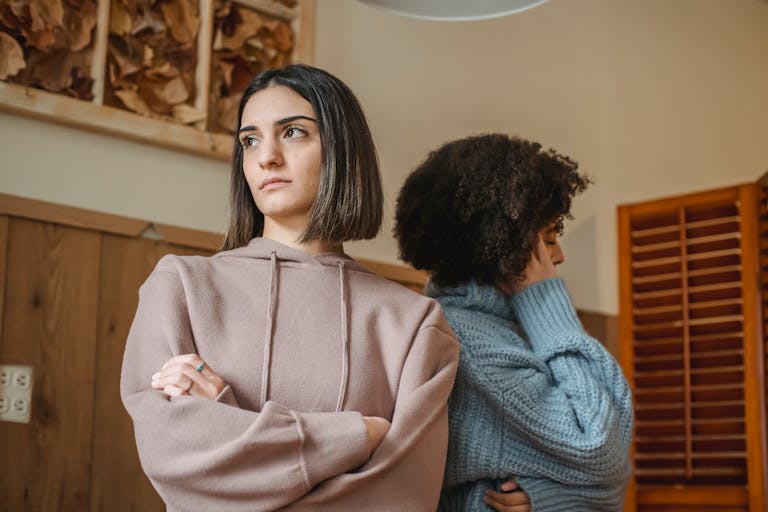 From below of unsatisfied multiracial women in casual clothes with crossed arms standing in light room during quarrel at home