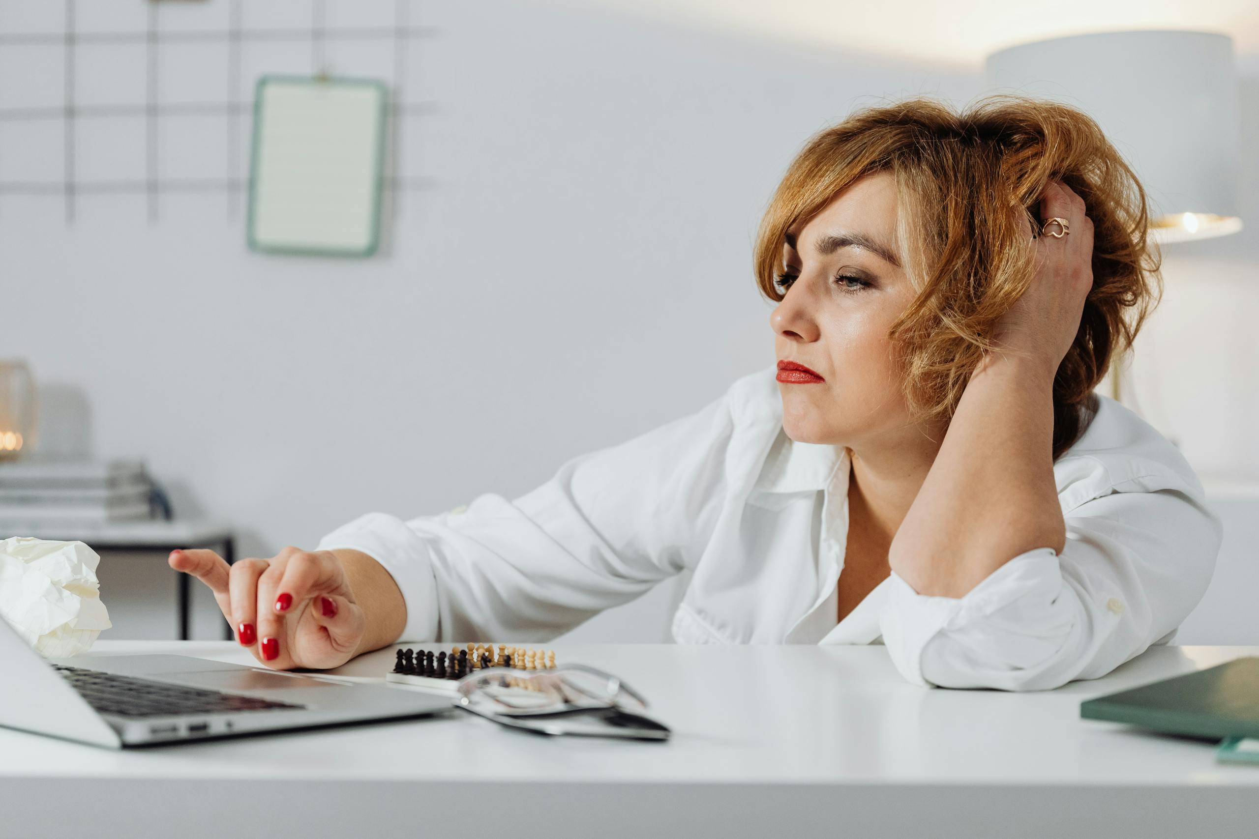 Frustrated woman at desk, using laptop with expression of stress. Indoors office environment.