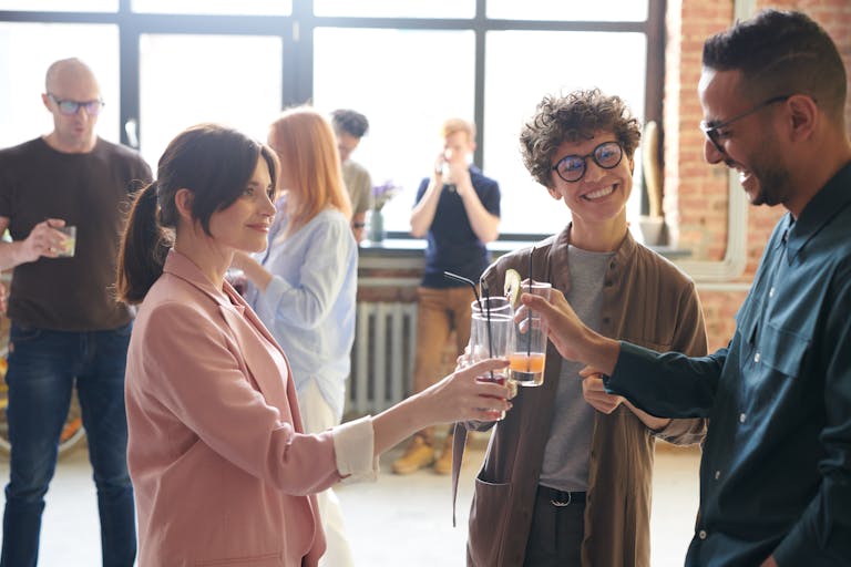 Group of diverse office colleagues enjoying drinks and a casual conversation in a bright workspace.