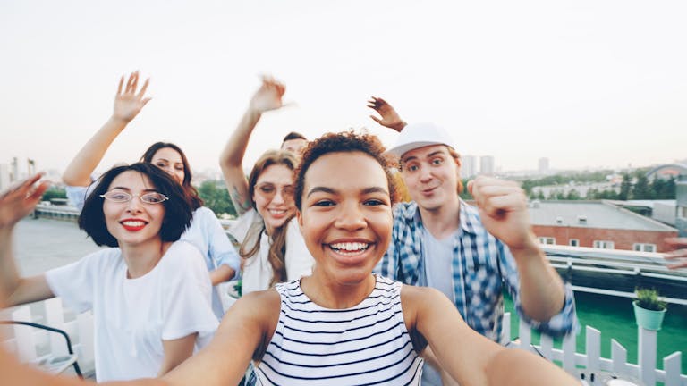 Group of friends enjoying a lively rooftop party together, smiling and waving.