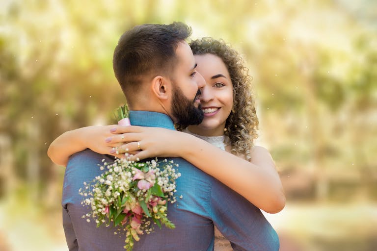 Happy couple embracing with a bouquet in a sunlit garden setting.