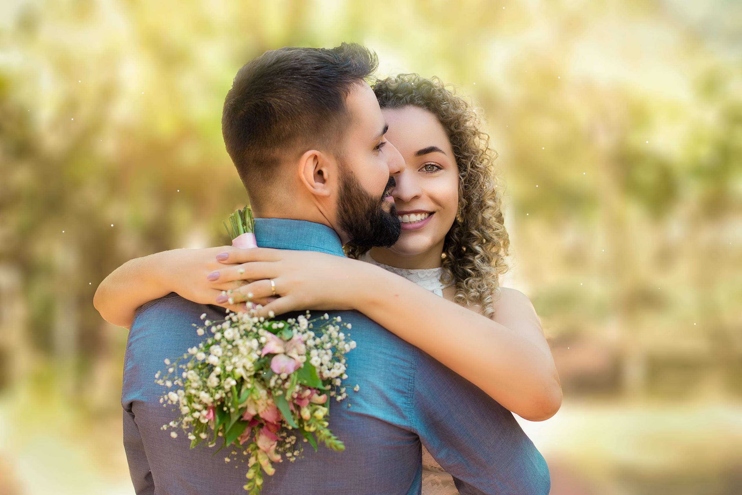 Happy couple embracing with a bouquet in a sunlit garden setting.