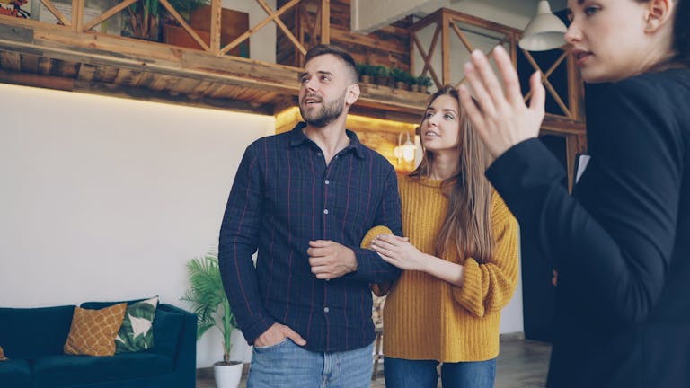 Happy couple exploring a stylish home with a real estate agent indoors.